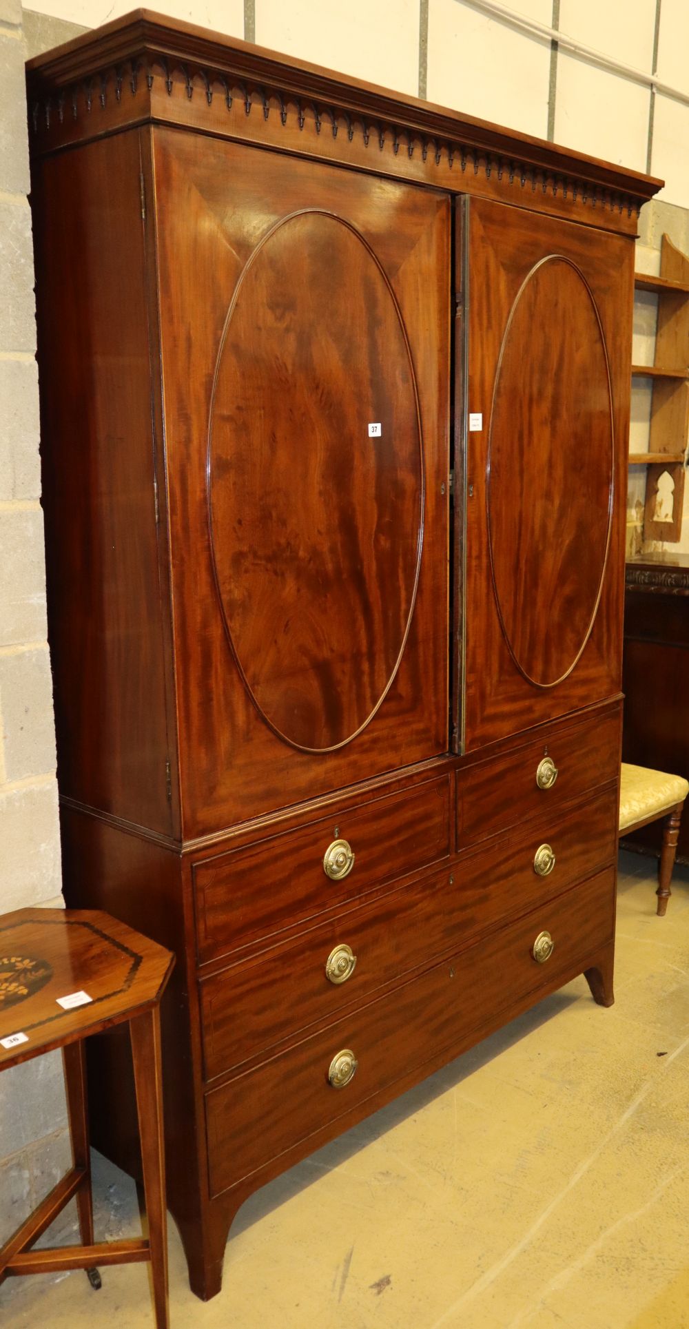 A Regency mahogany linen press, fitted oval panelled doors now enclosing hanging space to the left and five sliding trays to the right,